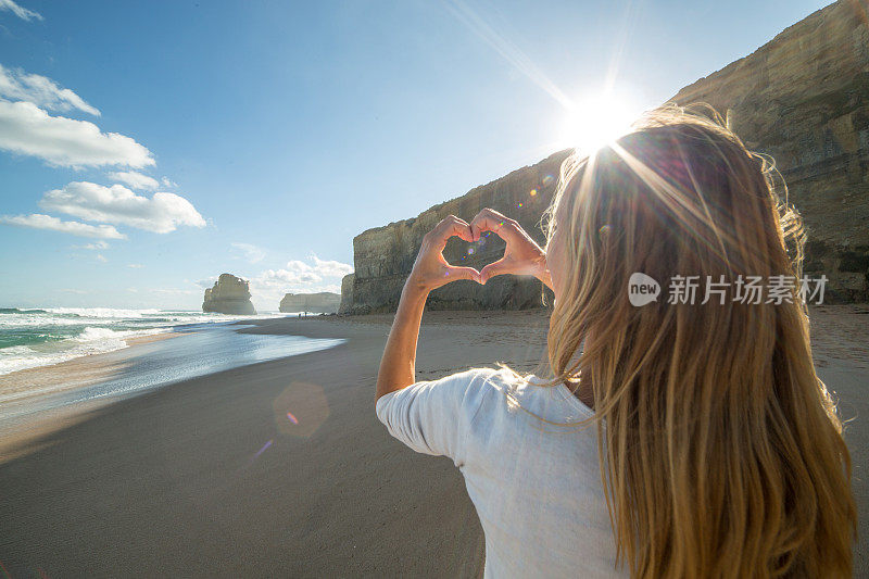 年轻女子在海滩上做心形手指架