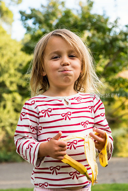 小女孩在公园里摆姿势吃香蕉
