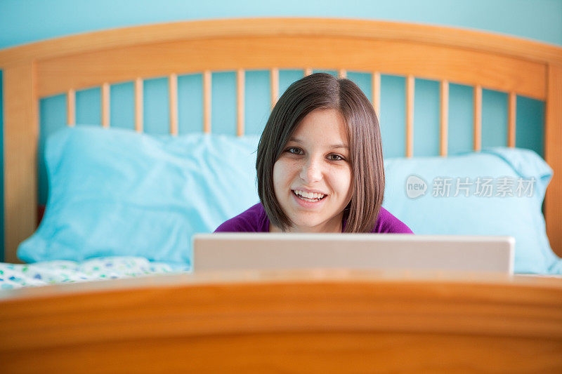 快乐的少女在床上用笔记本电脑工作