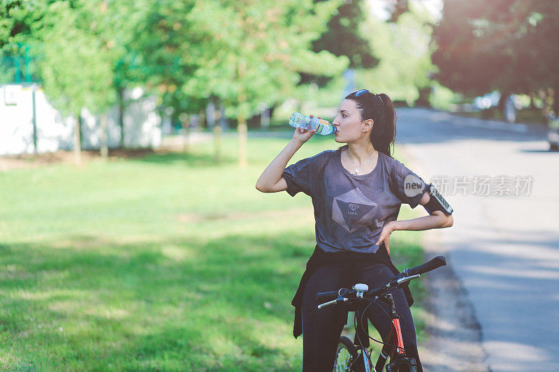 年轻女子在自行车上喝水