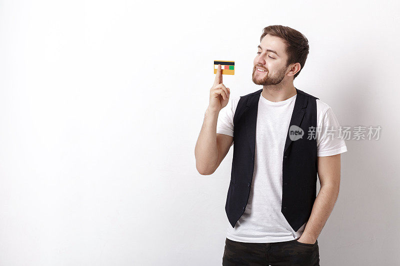 年轻英俊的男子胡子白衬衫和黑色马甲展示塑料信用卡和微笑