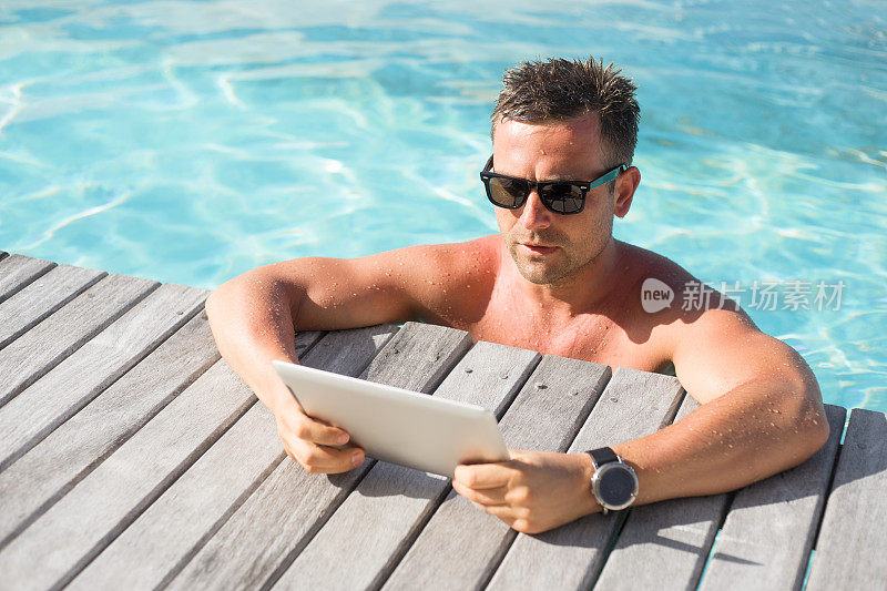 泳池边一个拿着平板电脑的男人