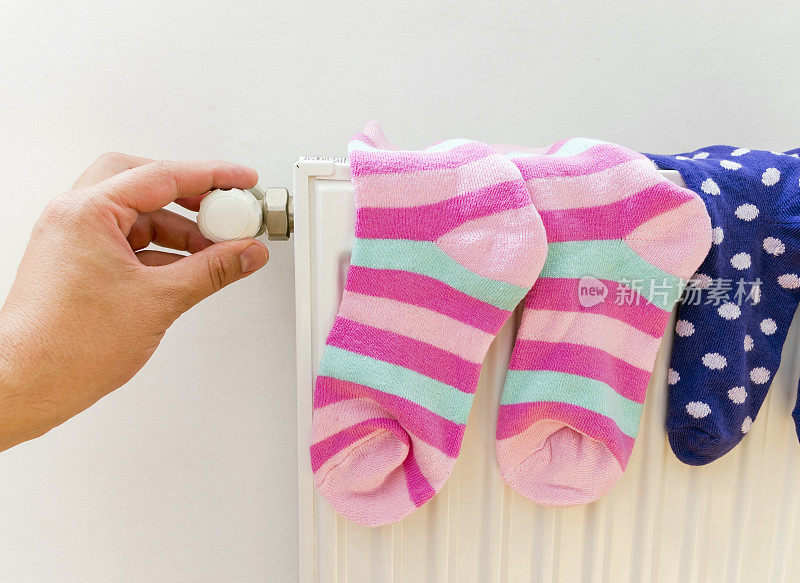 彩色袜子在散热器上烘干。在加热器上调节恒温器控制的人员。