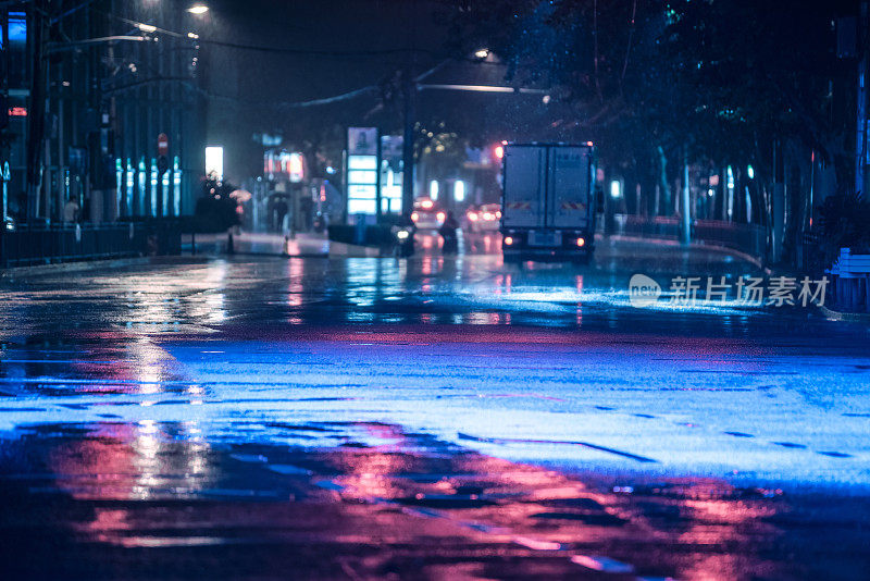 汽车在雨中行驶在潮湿的路面上，彩色的灯光反射在潮湿的柏油路上