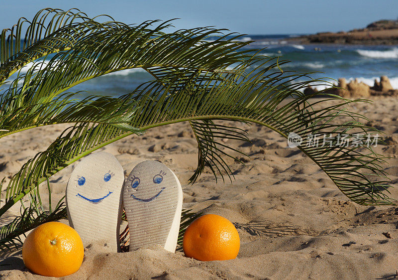 海边的沙滩拖鞋上画着笑脸，还有棕榈叶下的橘子