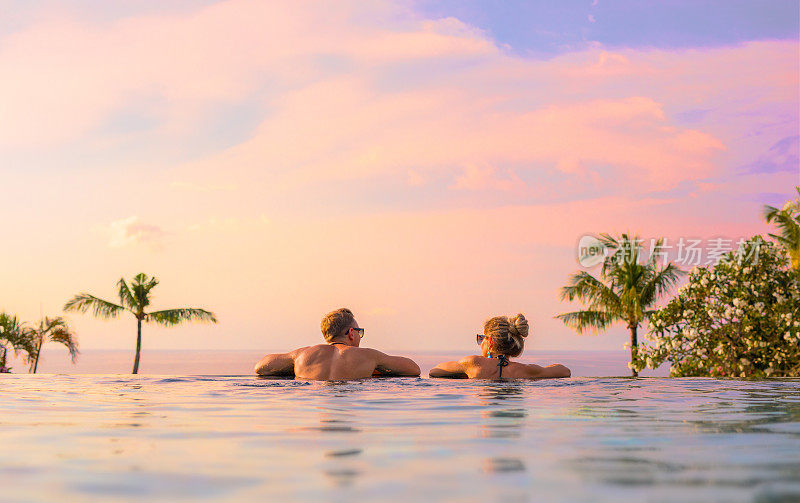 一对夫妇看美丽的日落在无限的游泳池