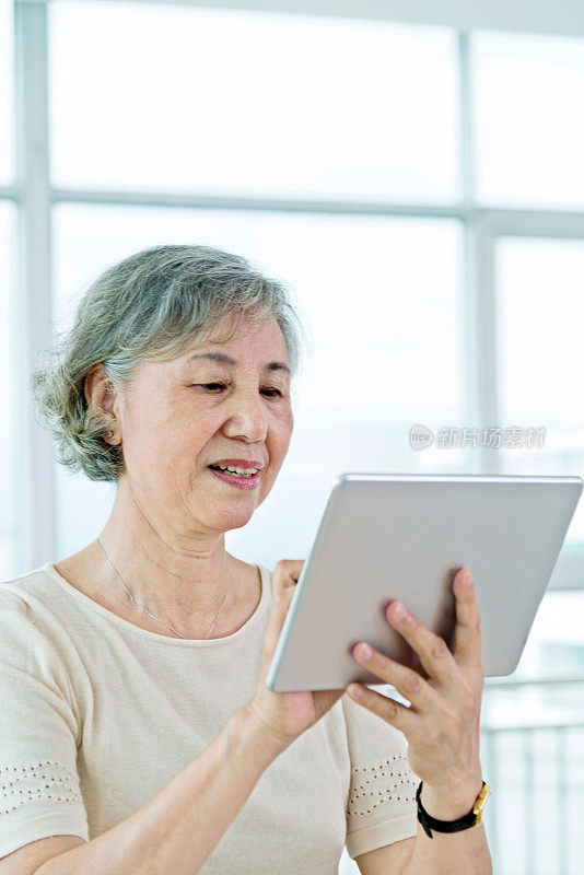 亚洲年长女性在家里使用数字平板电脑