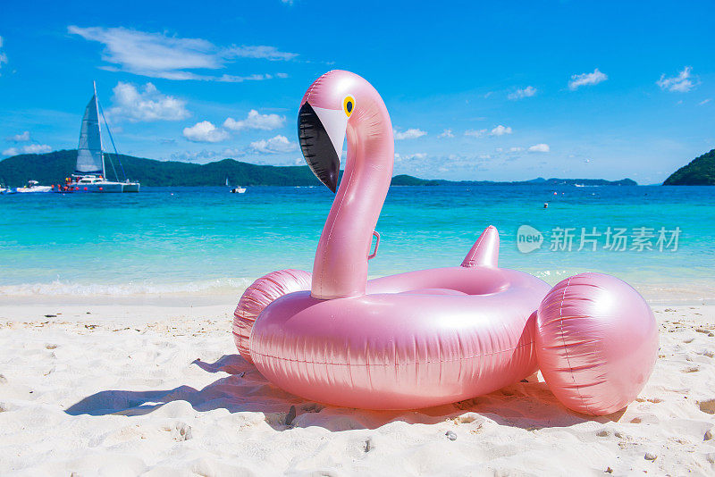 巨大的粉红色充气火烈鸟游泳池漂浮玩具在热带海滩上