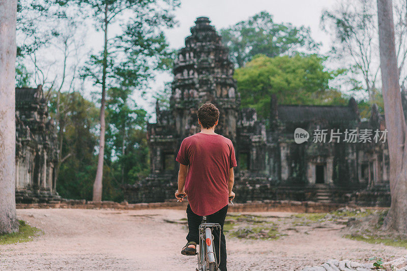 年轻的白人男子在吴哥窟骑自行车