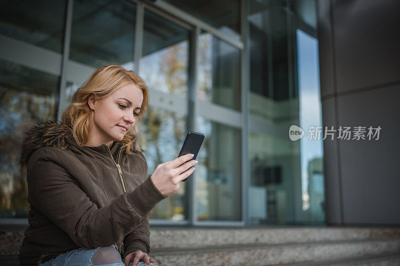 年轻女子在户外使用手机和阅读短信。