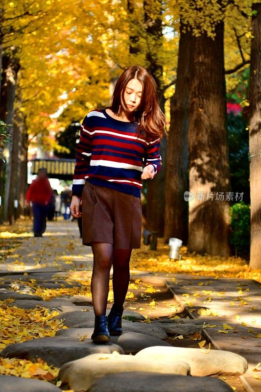 年轻的日本女人走在东京金黄色的银杏树下