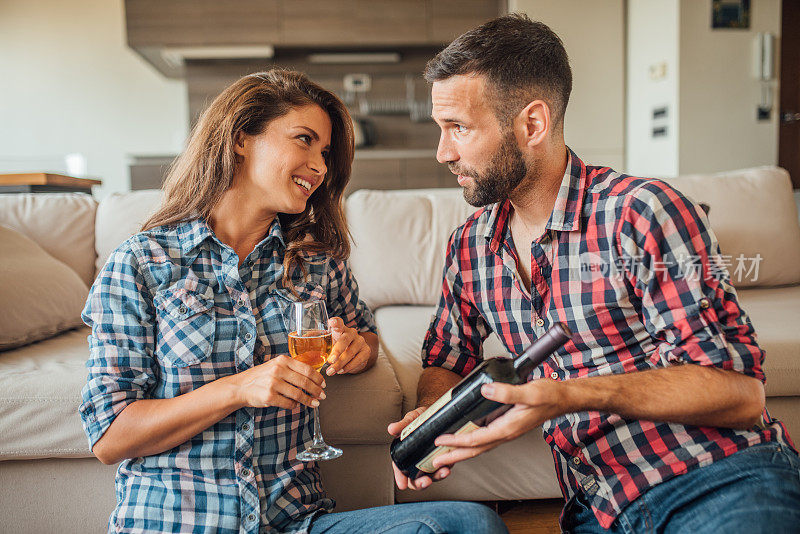 微笑的女人拿着酒杯，看着坐在她旁边拿着酒瓶的男人