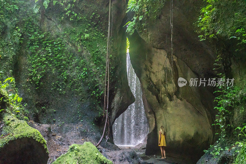 穿着黄色衣服的女孩站在热带雨林的洞穴里，仰望着从岩石上射下来的壮观的阳光。人们旅行的奇妙欲望自然的概念