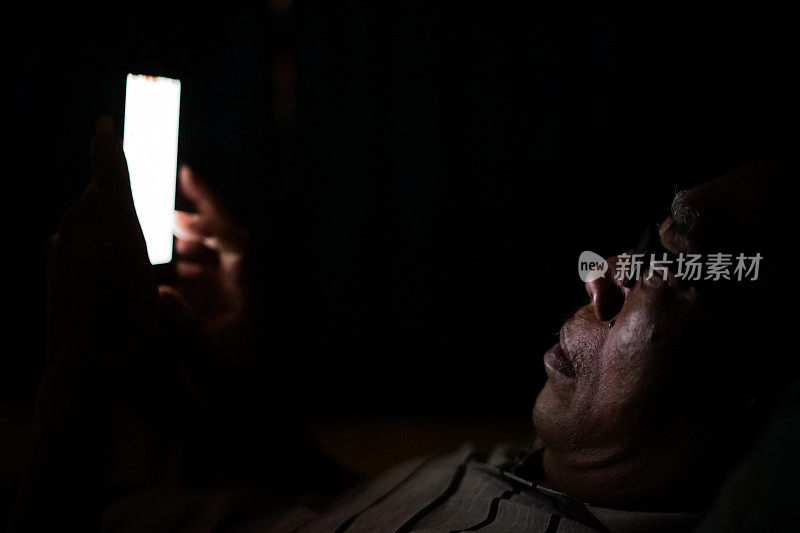 在暗室里玩智能手机的亚洲老人