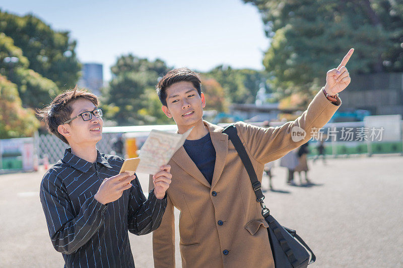 年轻的亚洲男子和日本朋友寻找旅游地点使用手机和花时间在亚洲旅行