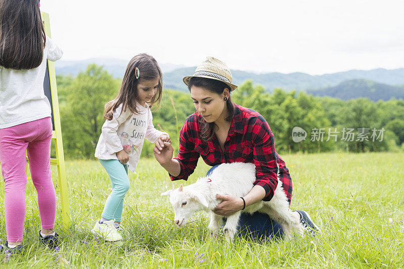 妈妈和女儿在和一只小山羊玩。