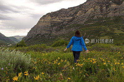 在春天的暴风雨中，一个女人走在峡谷前面的黄色野花地里