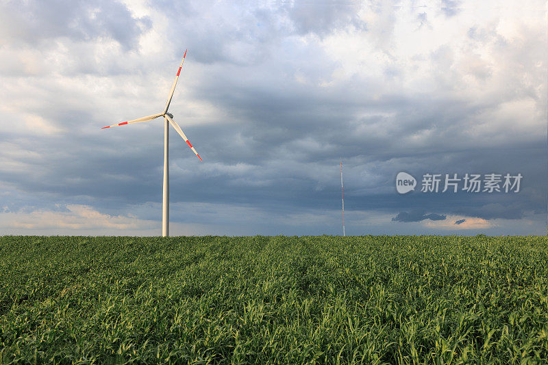 在阴沉的天空下，绿色的农田上安装着风力发电机