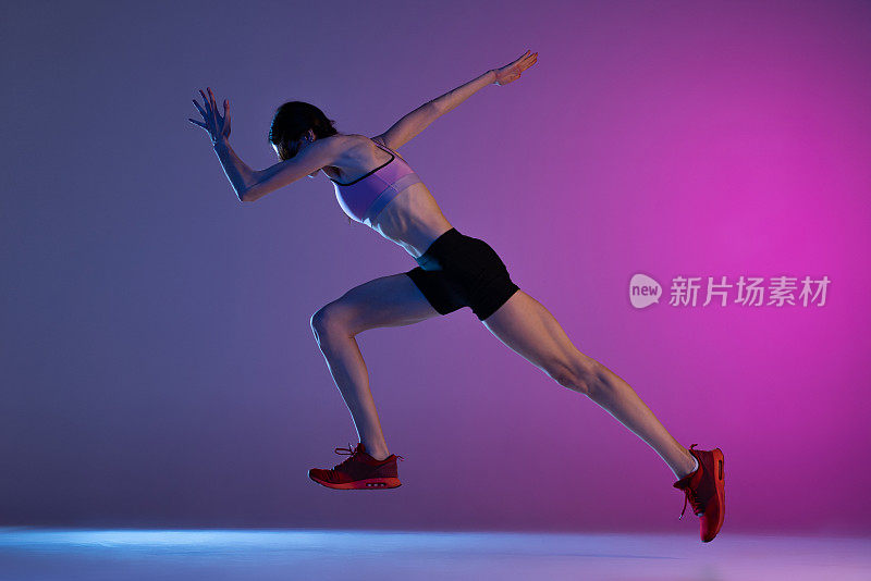 一个年轻的肌肉女孩，女跑步者或慢跑者训练孤立在粉红色的蓝色背景下的霓虹灯。体育、田径、竞技和积极的生活方式理念