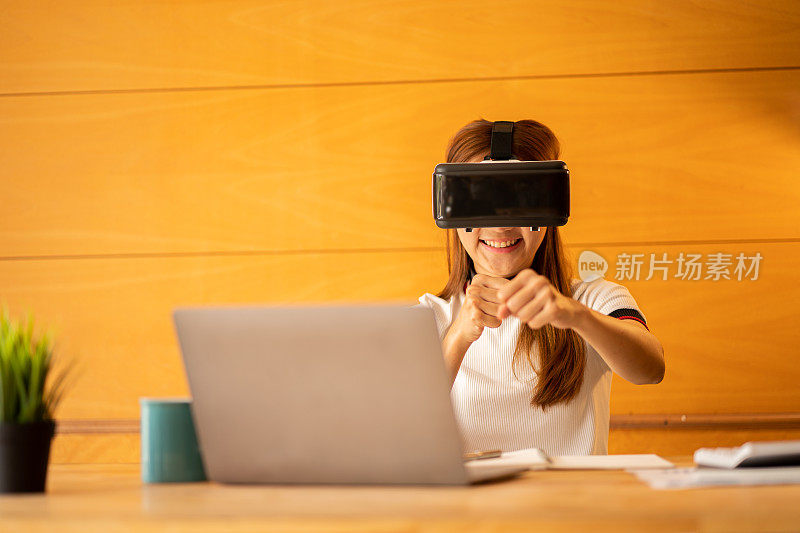 在家里戴着VR眼镜的开朗的白人女性。年轻女子享受眼镜与想象的手做想象的手势在虚拟现实设备在桌子上的笔记本电脑和计算器文件。