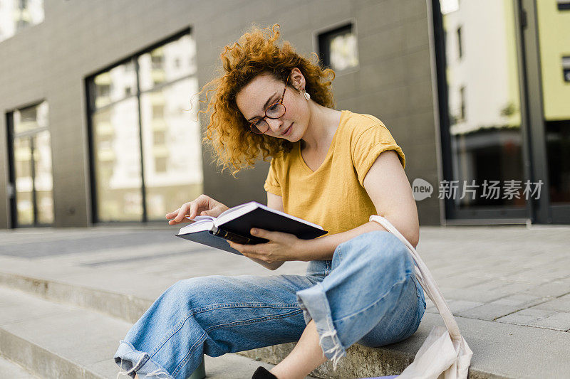 一个微笑的女大学生在户外读书的画像