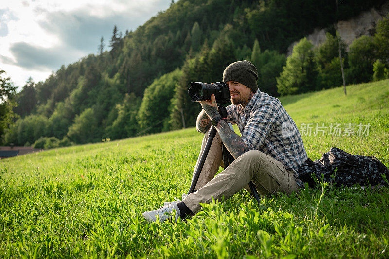 风景摄影师坐在草地上，用无反光镜相机拍摄大自然。