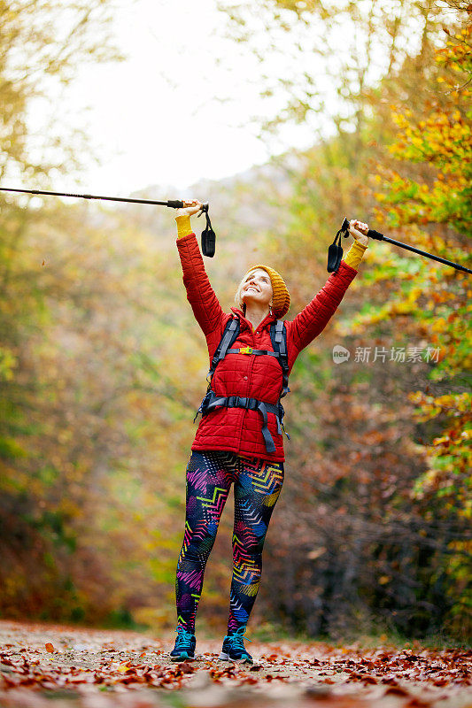徒步旅行的女孩与杆子和背包在一条小路上。举起手来享受大自然。秋季户外旅行和健康的生活方式。