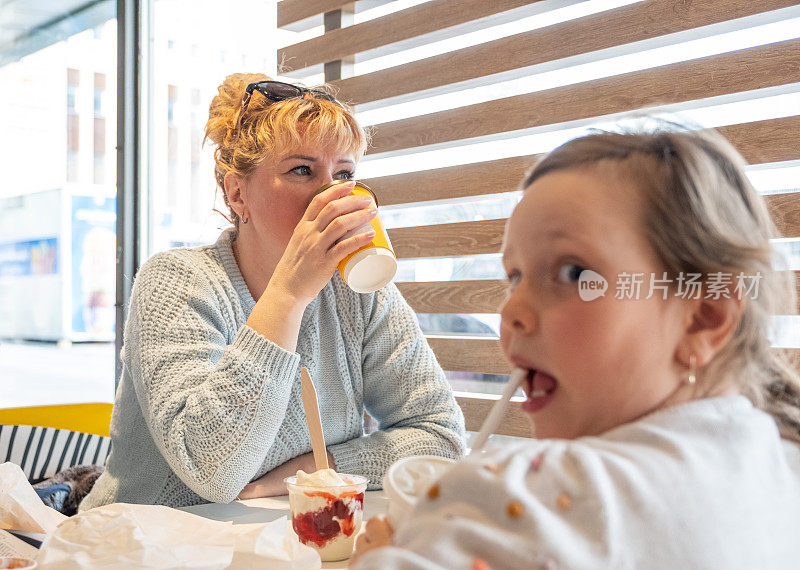 一名妇女用一次性杯子喝咖啡，一名7岁的白人女孩坐在那里喝咖啡。