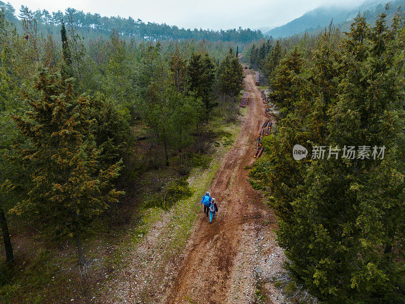 航拍老年夫妇背着背包在林地的土路上徒步