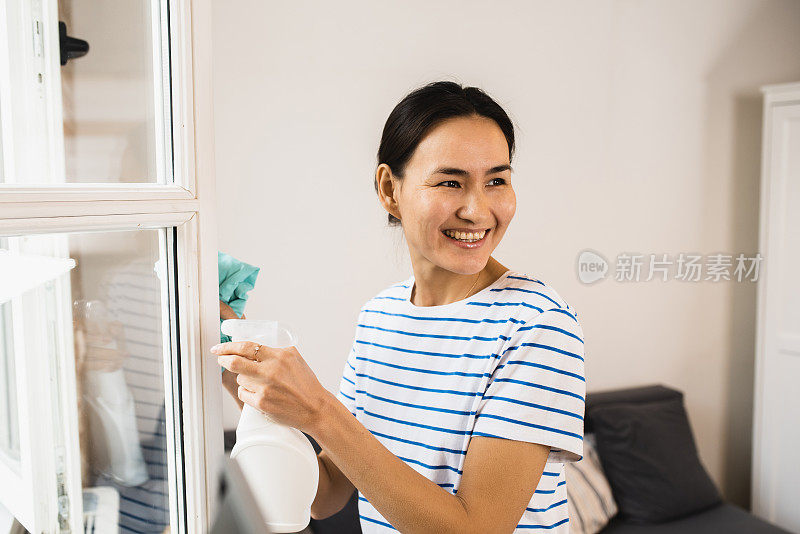 一个快乐的亚洲女人在家里擦窗户的画像