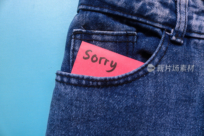 “对不起”这个词写在牛仔裤口袋里一张蓝色背景的红色便利贴上。道歉的概念