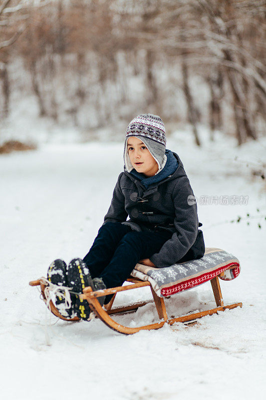 可爱的小男孩坐在雪橇上，在下雪天摆姿势