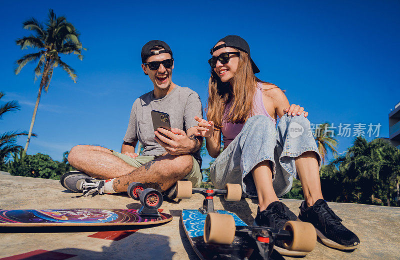 一对快乐的年轻情侣拿着滑板在滑板公园自拍