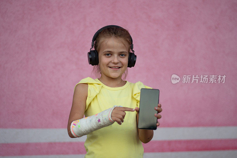 微笑的可爱小女孩的肖像，用智能手机打碎了耳机