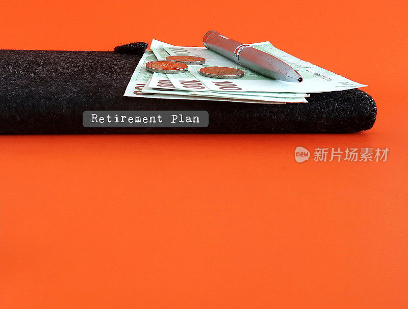 现金，黑色笔记本，笔在橙色复制空间背景文字退休计划-个人理财的概念-为退休储蓄的目标设定