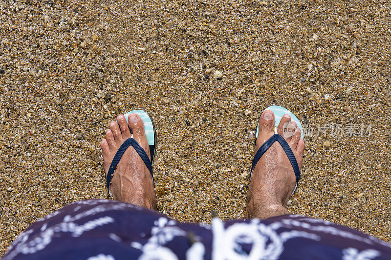 沙滩上男人穿着人字拖的脚。前视图。平的。本空间