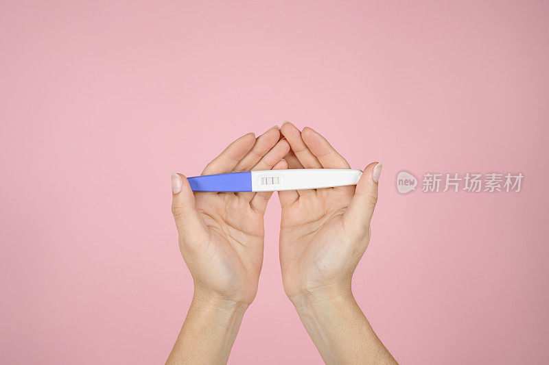 一名妇女的手在一个孤立的粉红色背景上拿着一个阳性的怀孕测试。母亲的概念
