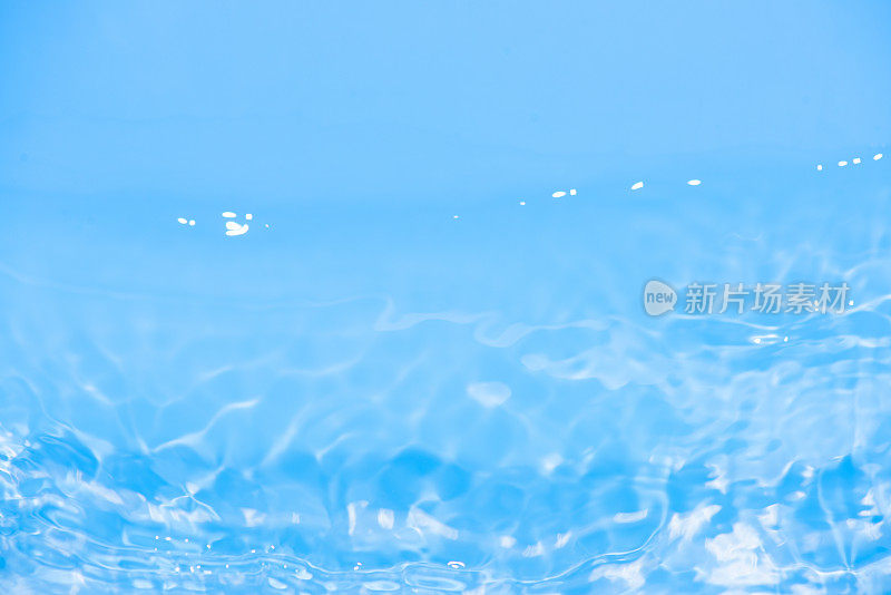 蓝水的波浪在水面上泛起模糊的涟漪。散焦模糊透明蓝色透明平静水面纹理与飞溅和泡沫。水波与闪亮的图案纹理背景。