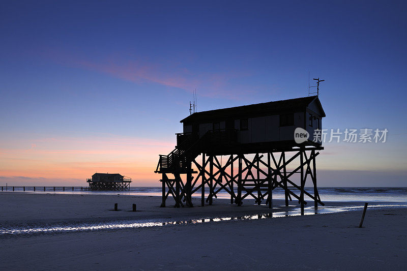 宁静的海岸日落，码头和沙滩上的棚屋