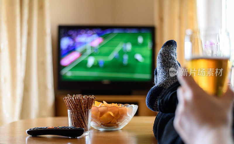 看电视(足球比赛)，脚放在桌子上，吃零食