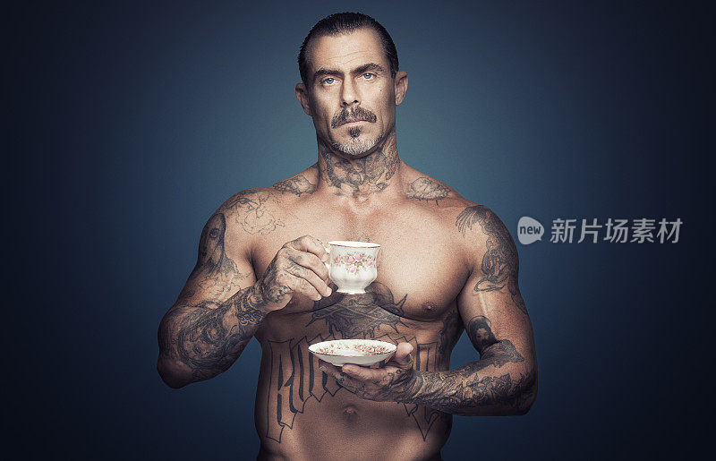 裸胸文身的男人拿着一杯茶。