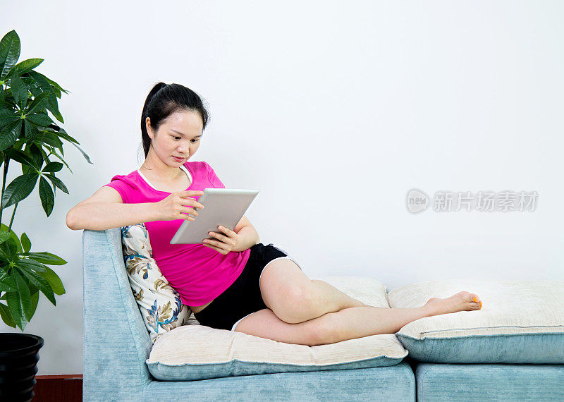 亚洲女性在沙发上使用平板电脑
