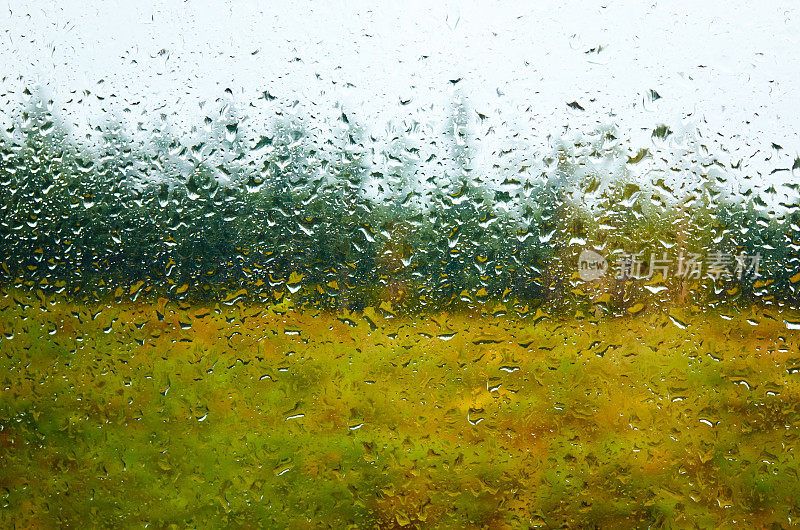 景观和多云的天空透过水滴雨潮湿的窗户