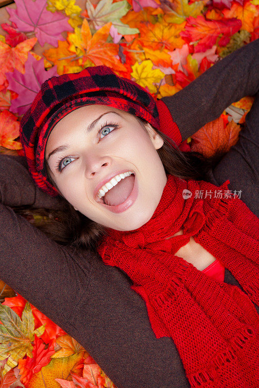 快乐的年轻女子躺在秋天的树叶上
