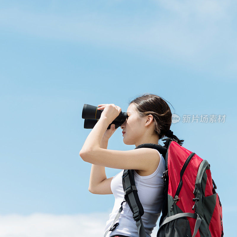 一名女性徒步旅行者用双筒望远镜望向山顶