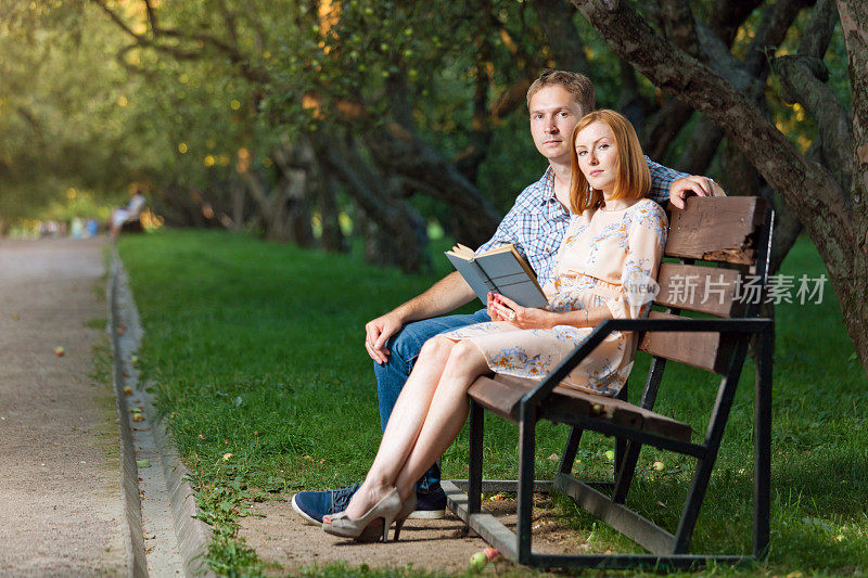 一对年轻夫妇在公园长椅上看书