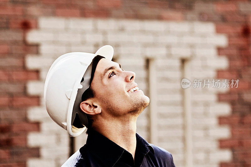 年轻的建筑工人戴着安全帽，抬头微笑着