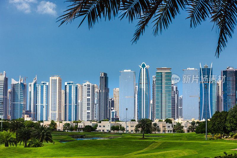 阿拉伯联合酋长国迪拜:高尔夫球道的前景现代摩天楼的JLT在背景，由枣棕榈叶框在顶部的图像-豪华的阿拉伯