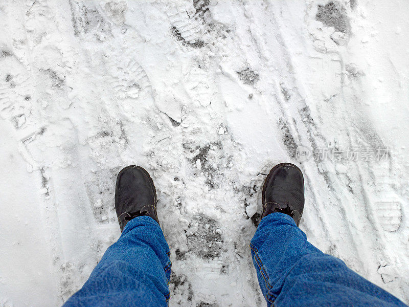脚踩在雪地里的柏油路上。