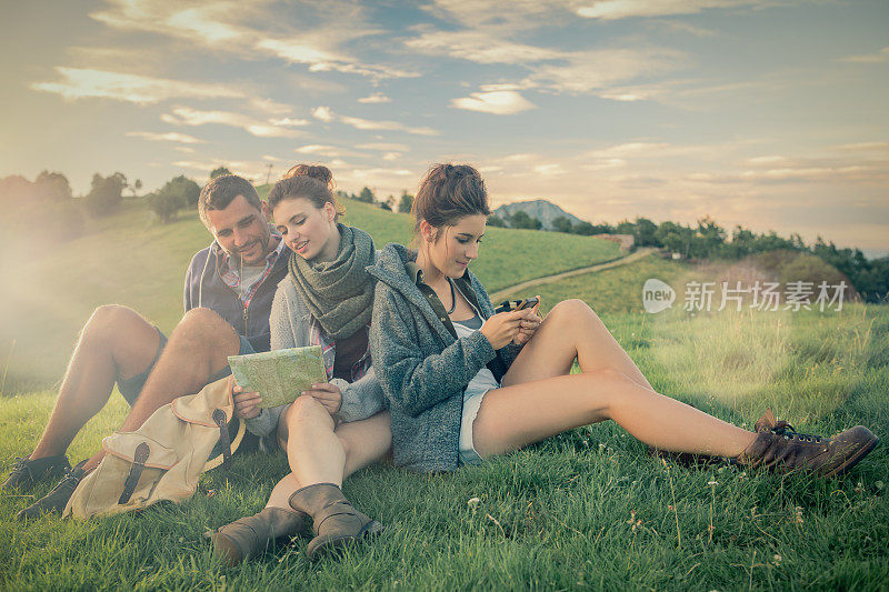 三个朋友坐在草地上看山上的地图